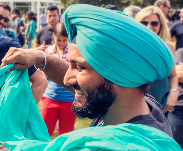Un uomo sorridente che indossa un turbante e sta avvolgendo il turbante di un’altra persona.