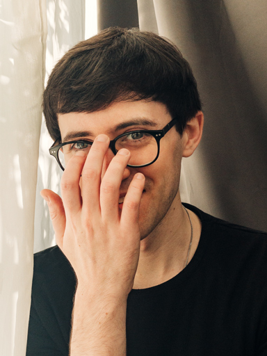 Un ritratto fotografico di Matthew che sorride mentre si sistema gli occhiali. 