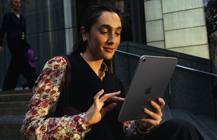 Pessoa sentada em uma escada em frente a um edifício grande usando um iPad Air de 11 polegadas cinza-espacial, com uma conexão Wi-Fi estável ao transitar entre redes
