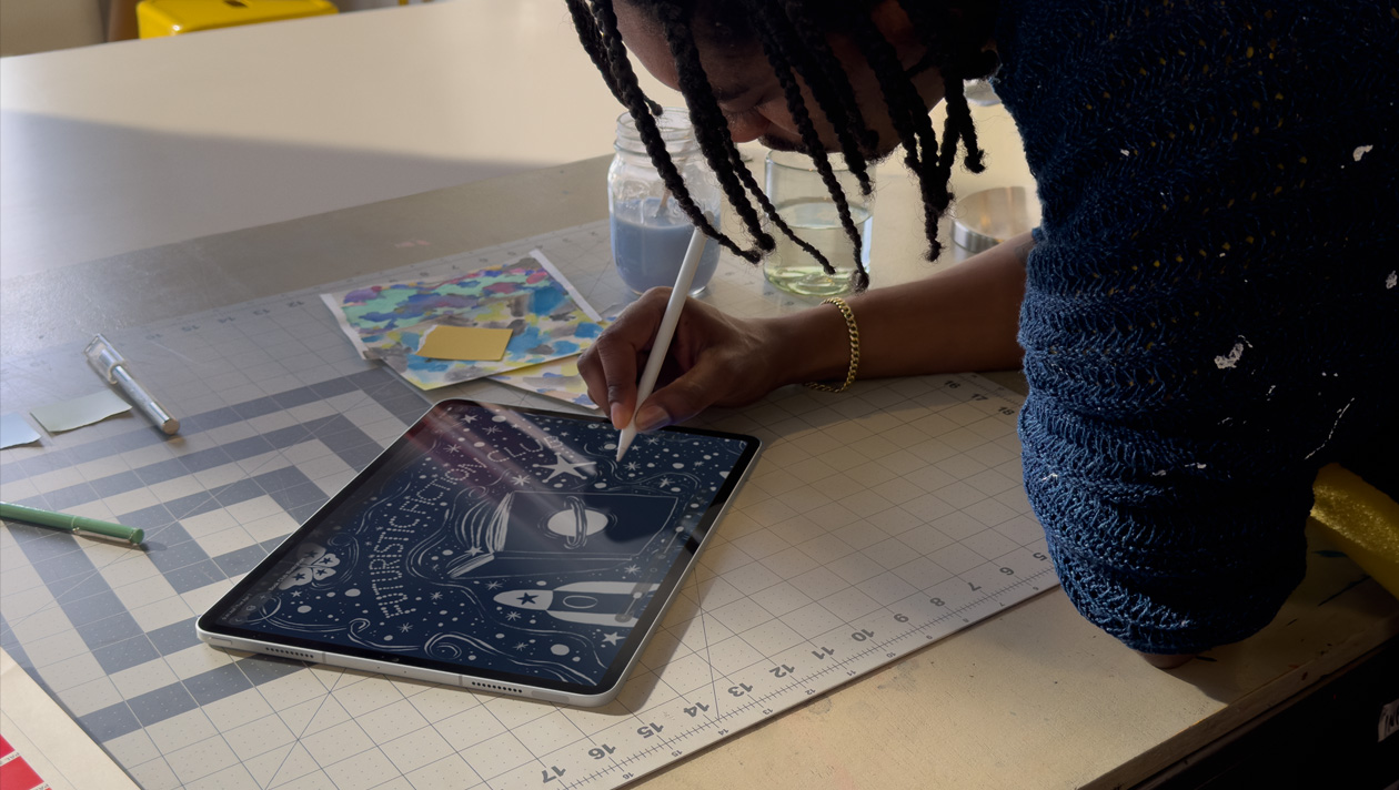 Saçları örgülü, mavi kazaklı bir kişi Apple Pencil ile iPad Pro’da çizim yapıyor, ekranda üzerinde gezegen olan bir kitap kapağı, bir gece gökyüzü illüstrasyonu, uzay gemisi, kelebek gösteriliyor ve merkezde fütüristik kurgu kitap kulübü yazıyor