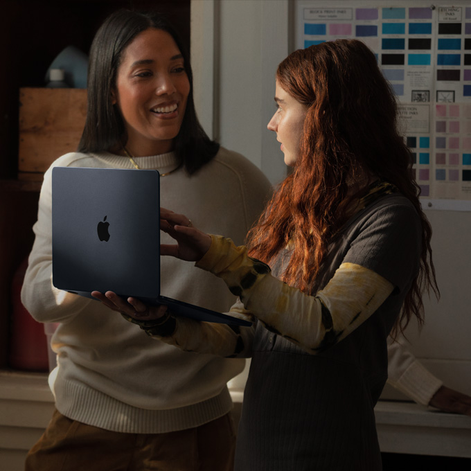 一名教師正和用手托著 MacBook 筆電的學生交談
